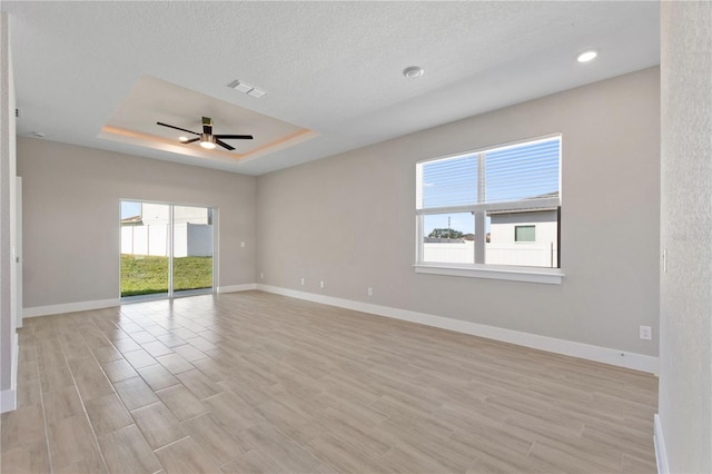 spare room with a tray ceiling, baseboards, light wood finished floors, visible vents, and a ceiling fan
