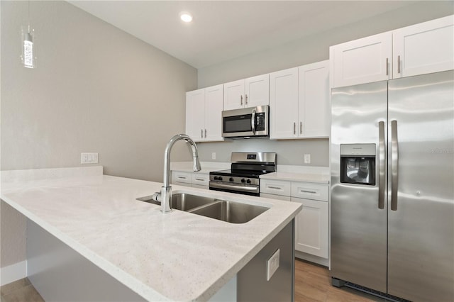 kitchen featuring light wood-type flooring, stainless steel appliances, a sink, white cabinets, and a peninsula