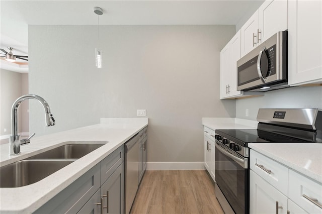 kitchen featuring stainless steel appliances, baseboards, hanging light fixtures, a sink, and light wood finished floors