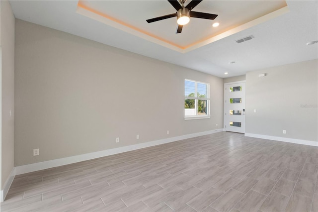 unfurnished room with a tray ceiling, baseboards, visible vents, and a ceiling fan