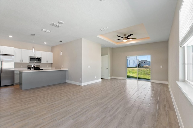 interior space with a tray ceiling, appliances with stainless steel finishes, open floor plan, visible vents, and ceiling fan