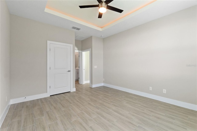 empty room featuring a tray ceiling, baseboards, visible vents, and a ceiling fan