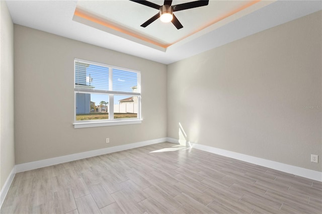 spare room with baseboards, ceiling fan, wood finished floors, and a raised ceiling