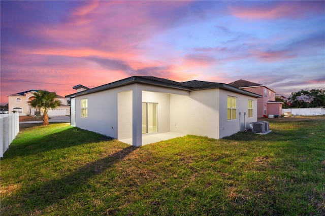 back of property with stucco siding, fence, central AC, and a yard