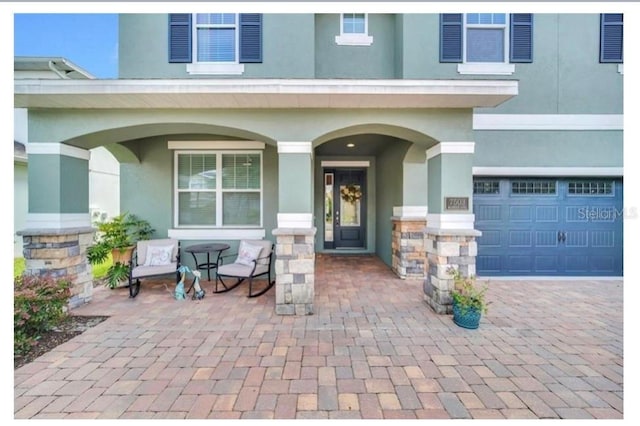 entrance to property with stucco siding, covered porch, a garage, and driveway