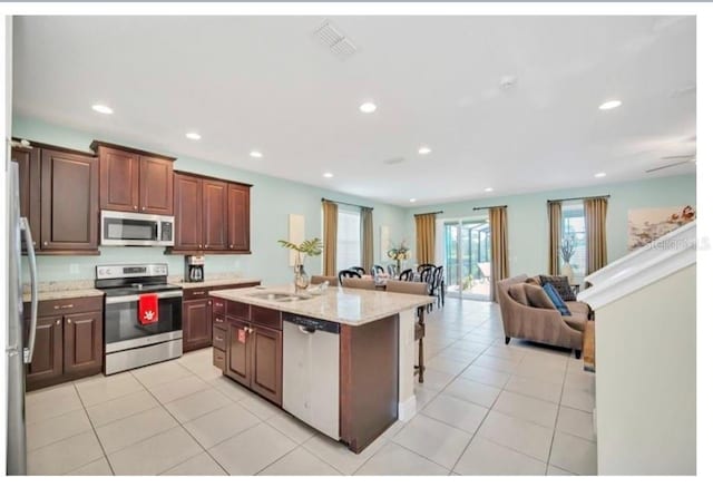 kitchen featuring appliances with stainless steel finishes, open floor plan, light tile patterned floors, a kitchen island with sink, and recessed lighting