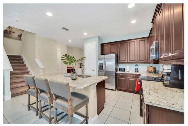 kitchen with light stone countertops, a kitchen breakfast bar, appliances with stainless steel finishes, light tile patterned floors, and visible vents
