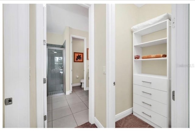 interior space featuring tile patterned floors, toilet, a stall shower, and baseboards