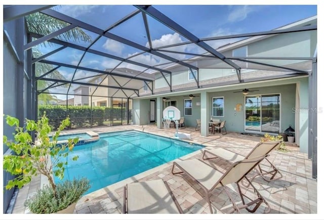 view of swimming pool featuring glass enclosure, a pool with connected hot tub, a ceiling fan, and a patio area