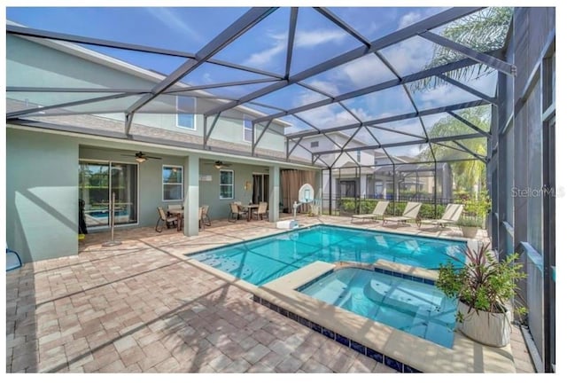 view of pool featuring a pool with connected hot tub, glass enclosure, ceiling fan, and a patio