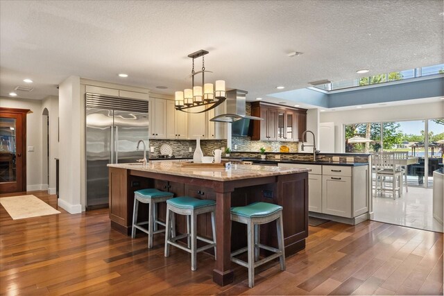 7849 Georgeann St, Winter Park, FL 32792 - kitchen featuring stainless steel built in fridge, an island with sink, wall chimney range hood, a sink, and dark wood finished floors