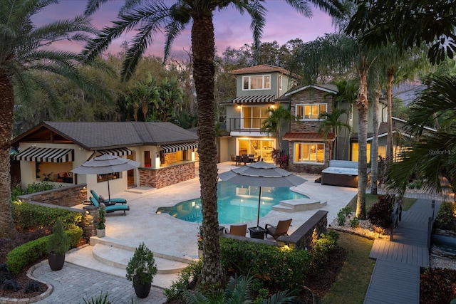 7849 Georgeann St, Winter Park, FL 32792 - back of house at dusk with stucco siding, a balcony, stone siding, a hot tub, and a patio area