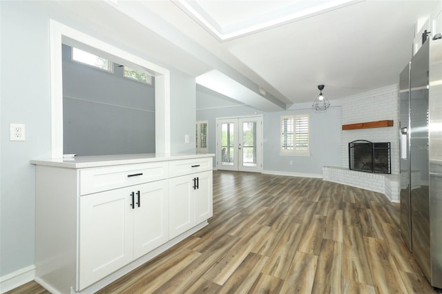 unfurnished living room with french doors, wood finished floors, baseboards, and a brick fireplace