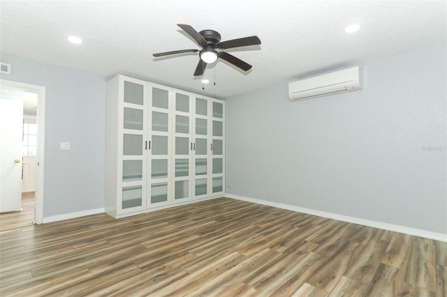 spare room with ceiling fan, wood finished floors, and a wall mounted air conditioner