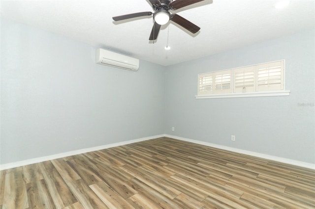 empty room with a wall mounted air conditioner, baseboards, and wood finished floors