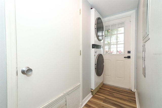 laundry room with laundry area, wood finished floors, stacked washer / drying machine, and baseboards