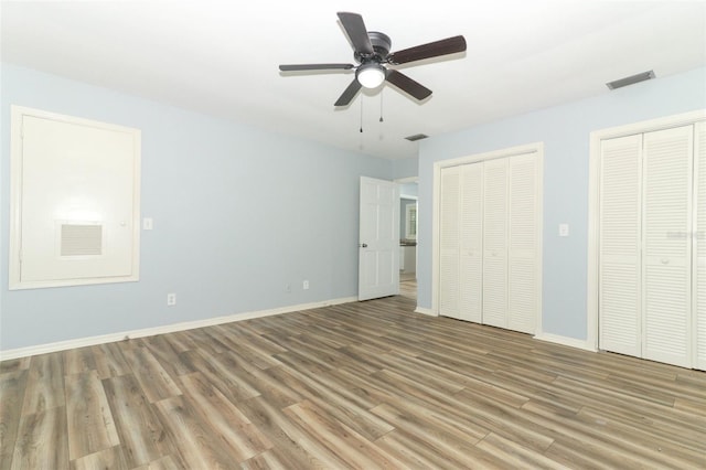 unfurnished bedroom featuring wood finished floors, baseboards, visible vents, and multiple closets