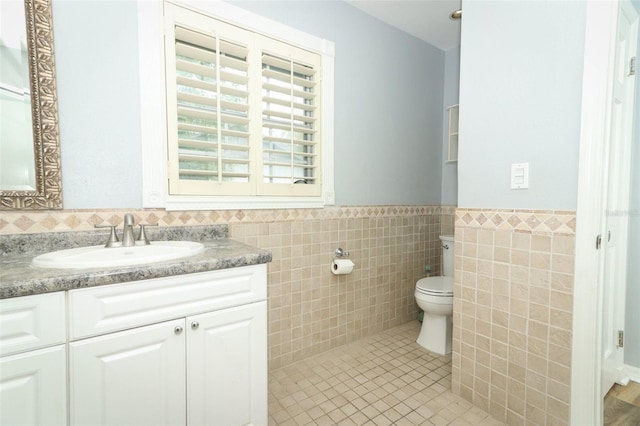 bathroom with vanity, tile patterned floors, toilet, a wainscoted wall, and tile walls