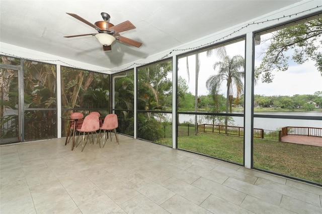 unfurnished sunroom with a healthy amount of sunlight, a ceiling fan, and a water view