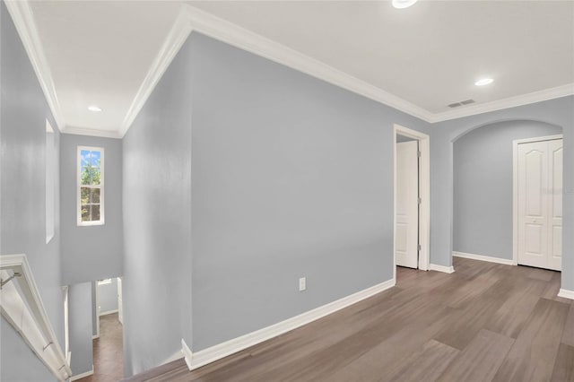 spare room featuring baseboards, crown molding, visible vents, arched walkways, and wood finished floors