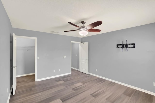unfurnished bedroom with visible vents, baseboards, a closet, a walk in closet, and wood finished floors