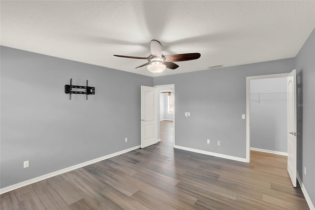 unfurnished bedroom featuring a spacious closet, baseboards, ceiling fan, and wood finished floors