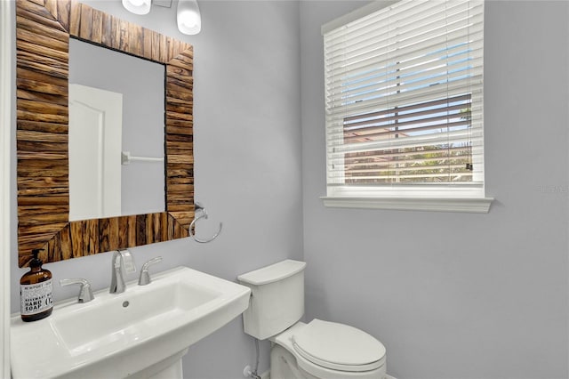 half bathroom with baseboards, a sink, and toilet