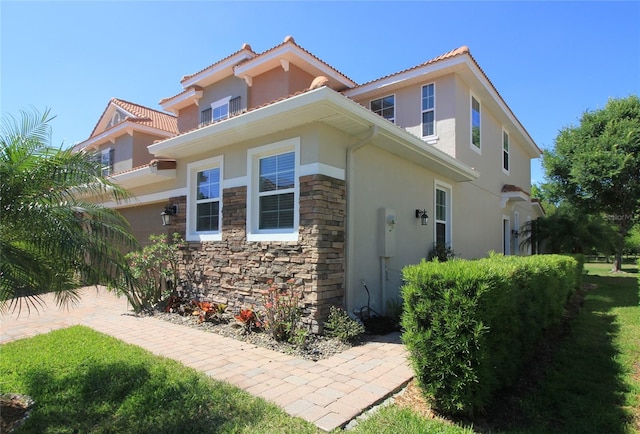 view of side of home featuring a tiled roof, stone siding, and stucco siding
