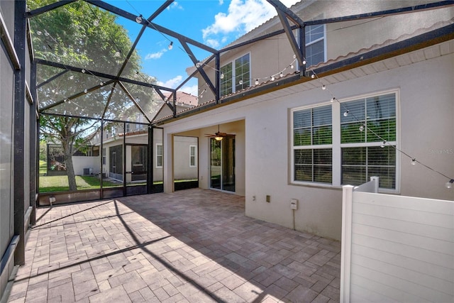 rear view of property with ceiling fan, a patio area, stucco siding, and glass enclosure