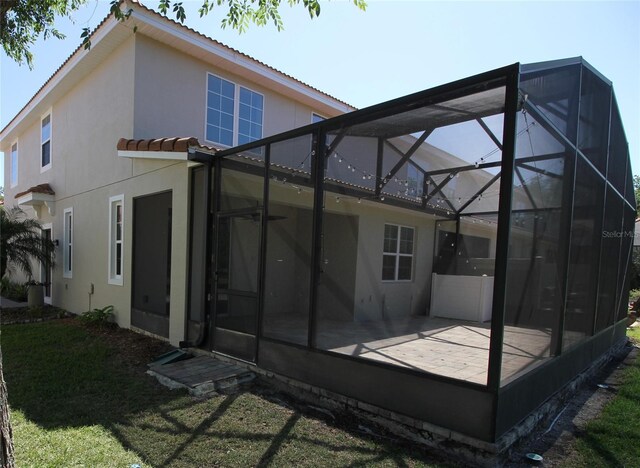 rear view of house with a yard, a tile roof, glass enclosure, and stucco siding