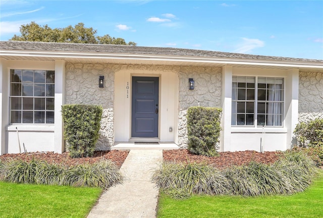 doorway to property with stucco siding and roof with shingles