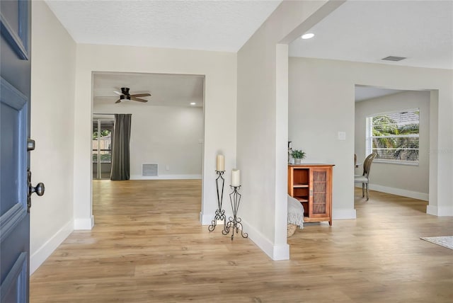 corridor with light wood-style flooring, a textured ceiling, baseboards, and visible vents