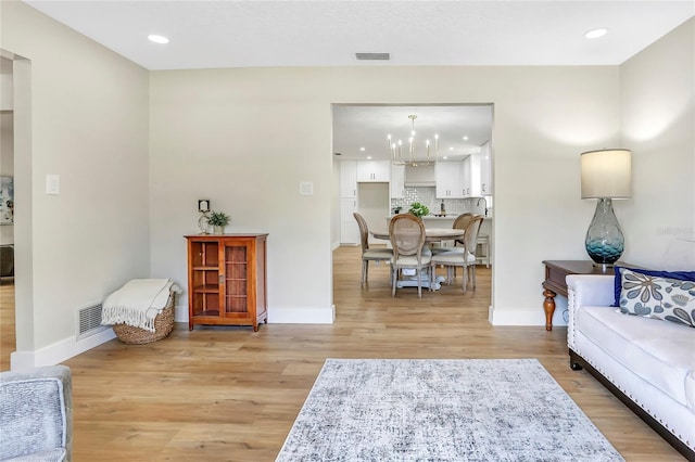 living room featuring baseboards, light wood-style flooring, visible vents, and an inviting chandelier