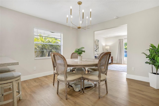 dining space with plenty of natural light, a notable chandelier, baseboards, and light wood-style floors