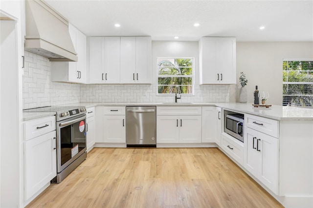 kitchen featuring custom range hood, a sink, light wood finished floors, a peninsula, and appliances with stainless steel finishes