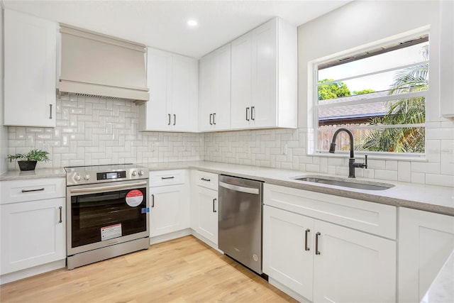 kitchen with backsplash, a sink, light wood-style flooring, stainless steel appliances, and white cabinets