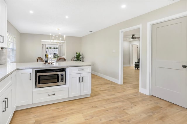 kitchen featuring white cabinets, a peninsula, light wood-type flooring, stainless steel microwave, and decorative light fixtures