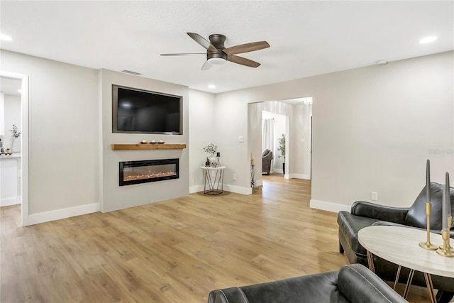 living area with light wood finished floors, a glass covered fireplace, baseboards, ceiling fan, and recessed lighting