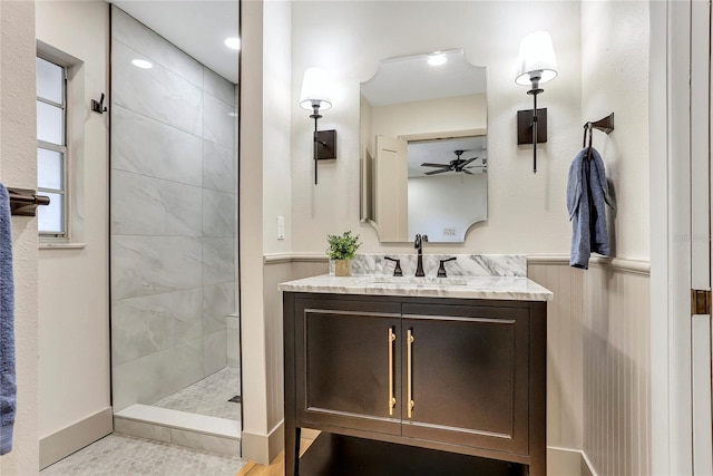 bathroom with vanity, a wainscoted wall, tiled shower, and a ceiling fan