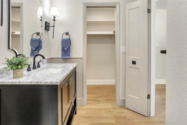 bathroom featuring a wainscoted wall, wood finished floors, a walk in closet, and vanity