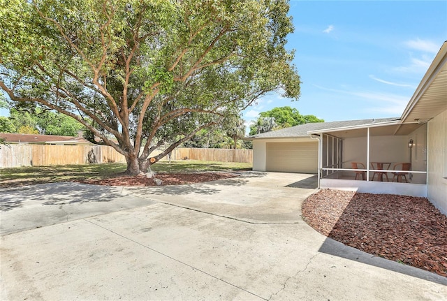 view of patio / terrace featuring a sunroom, concrete driveway, fence, and an attached garage