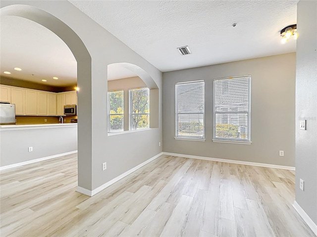 10852 Spider Lily Dr Unit S, Orlando, FL 32832 - unfurnished living room with light wood-style flooring, baseboards, a textured ceiling, recessed lighting, and arched walkways
