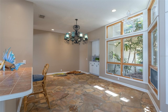 unfurnished dining area featuring recessed lighting, a chandelier, stone flooring, baseboards, and visible vents