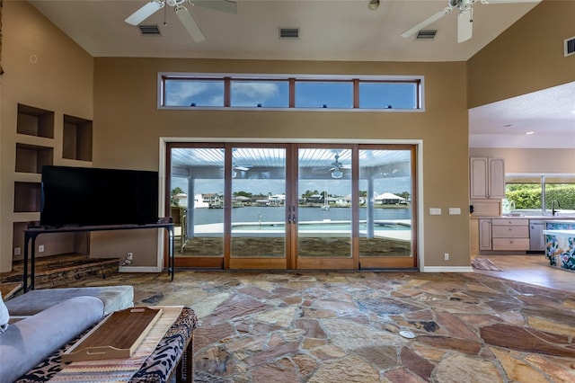 living area featuring ceiling fan, a high ceiling, and stone floors