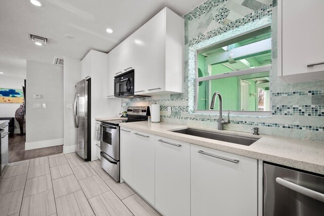 kitchen with visible vents, stainless steel appliances, tasteful backsplash, white cabinetry, and a sink