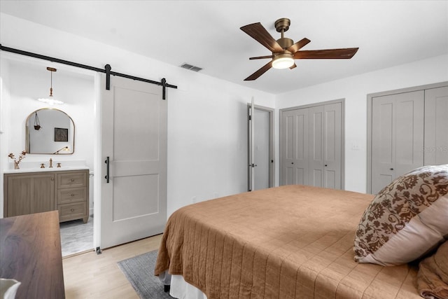 1558 Regal Oak Dr, Kissimmee, FL 34744 - bedroom featuring a barn door, multiple closets, ensuite bathroom, light wood-type flooring, and visible vents