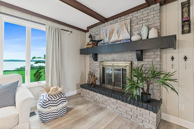 living room with a water view, baseboards, beamed ceiling, a brick fireplace, and wood finished floors