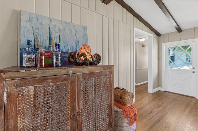 foyer with lofted ceiling with beams, a dry bar, wood finished floors, and wooden walls