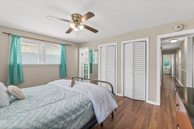 bedroom featuring baseboards, ceiling fan, two closets, and dark wood finished floors