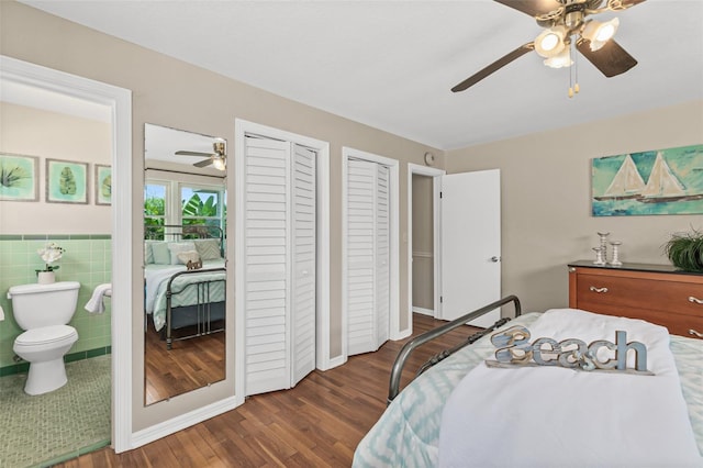 bedroom with ensuite bathroom, multiple closets, tile walls, wood finished floors, and a ceiling fan